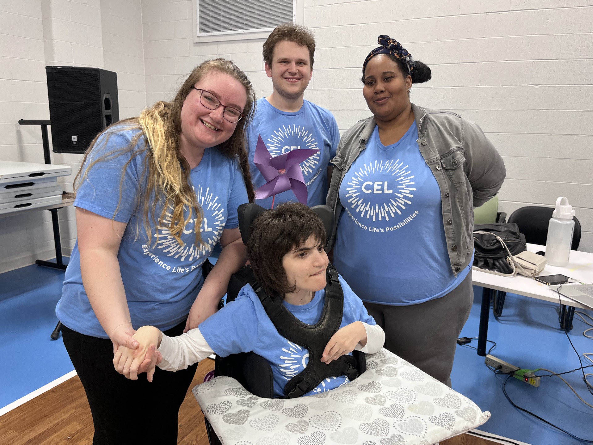 REACH adult day program members posing with staff smiling as they wear their Blue CEL T-shirts in CEL gym.