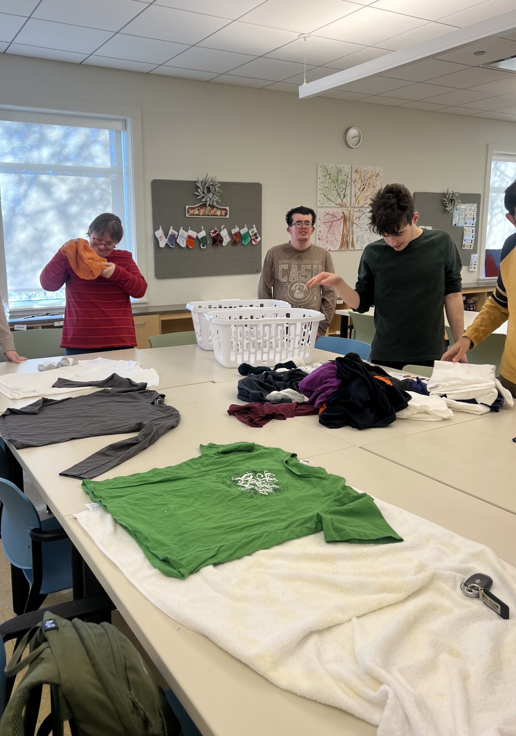 Group of Catalyst members, one woman and two men, holding clothes and laundry on a table, focused on folding tasks inside the CEL building.