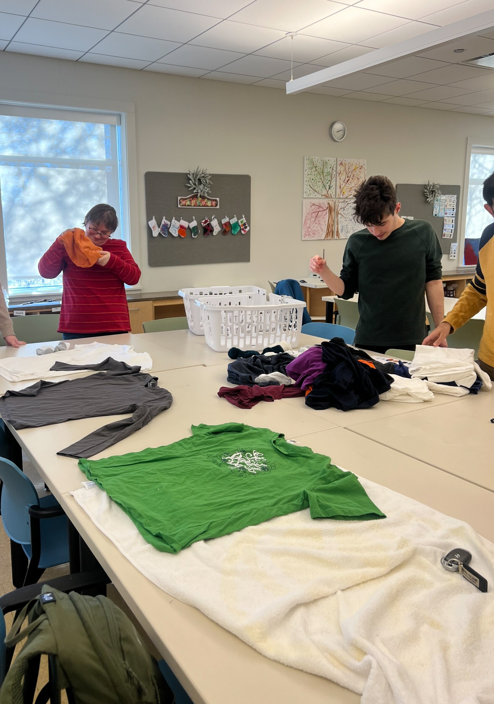 Group of Catalyst members, one woman and two men, holding clothes and laundry on a table, focused on folding tasks inside the CEL building.