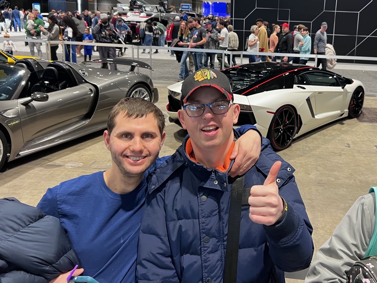 Two CEL male REACH members smiling at the Chicago Auto Show with two vehicles in the background.