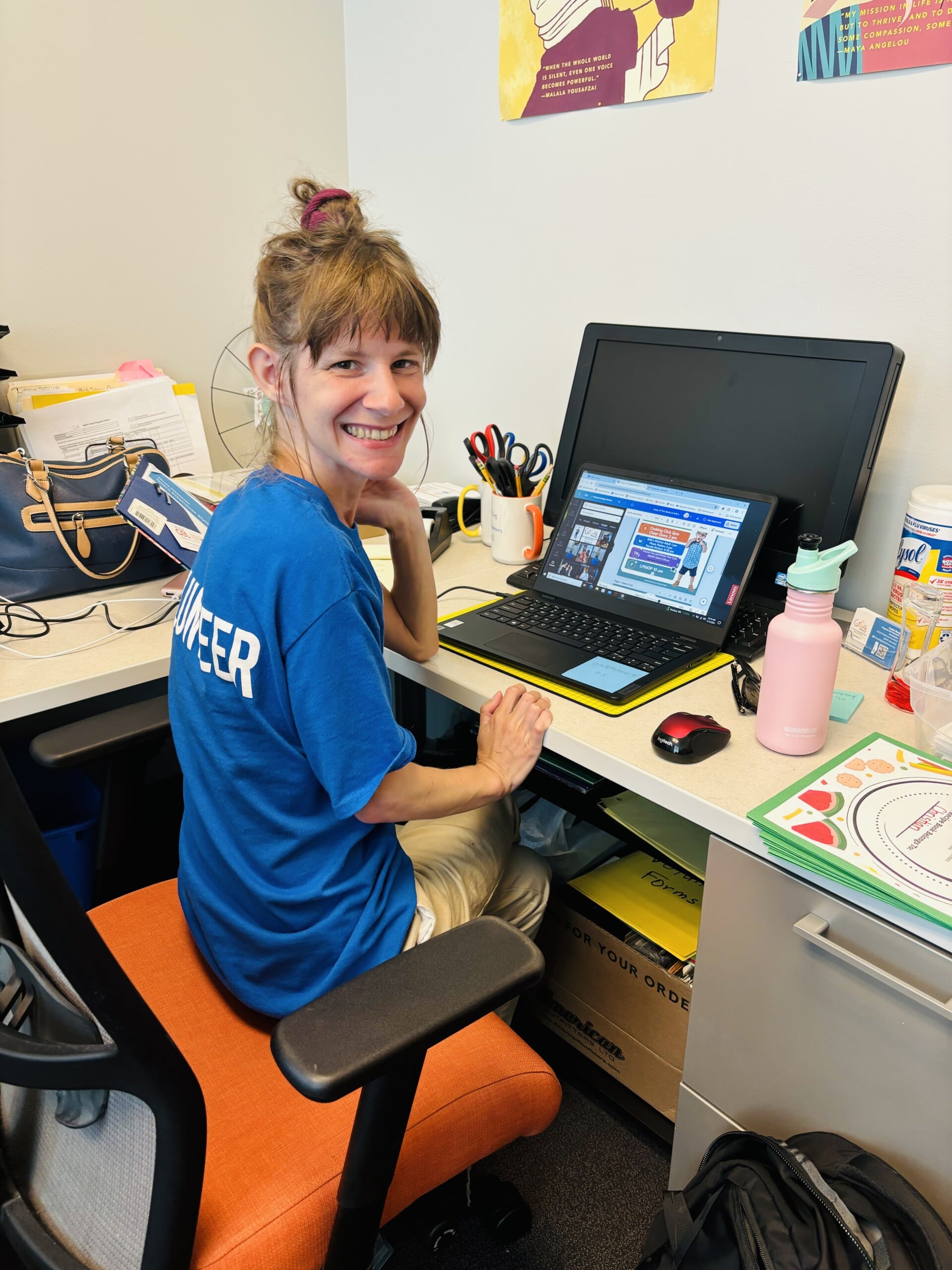 Employment Member Melissa G working in the office at Gigi's Playhouse as a marketing assistant. She is using her open laptop to create a graphic in Canva.