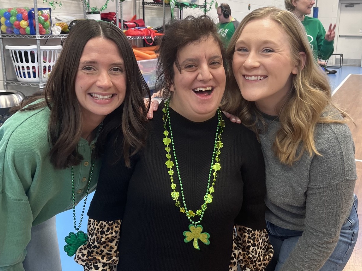 CEL staff posing with member smiling at St. Patrick's Day Party in the gym.