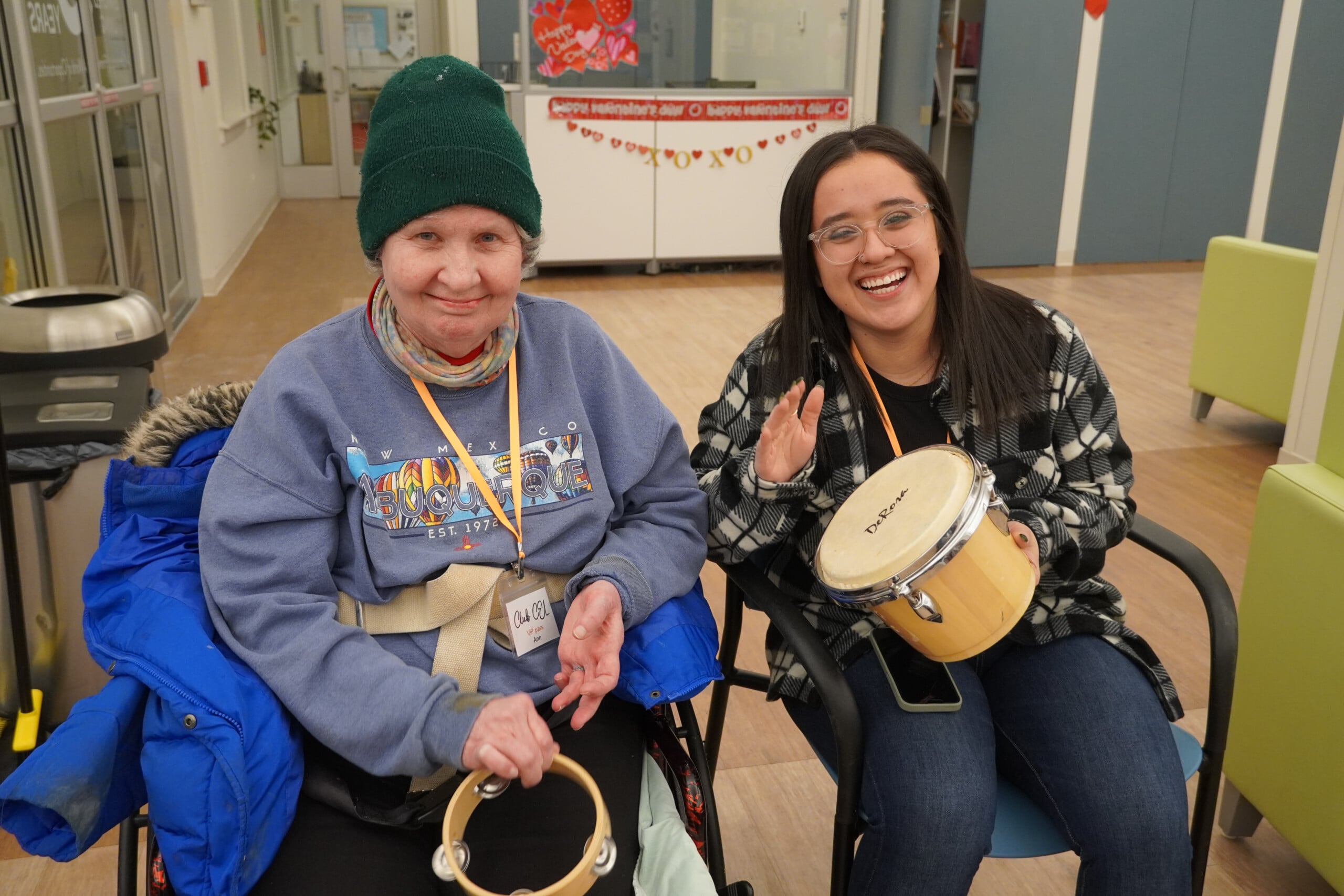 A picture of Friday Night music member playing tambourine while volunteer plays drums both smiling.
