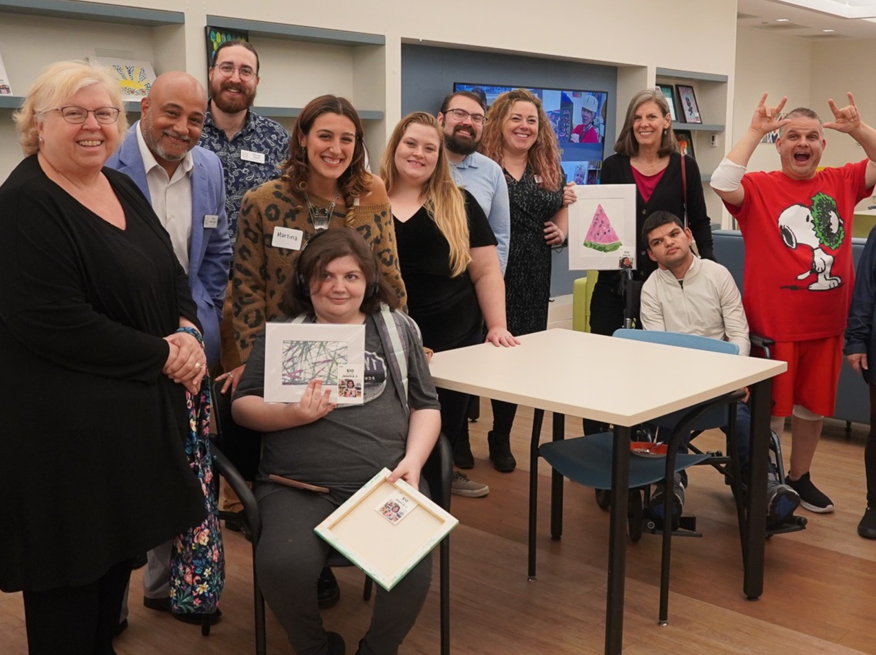 Members and their families pose for a photo and hold up art
