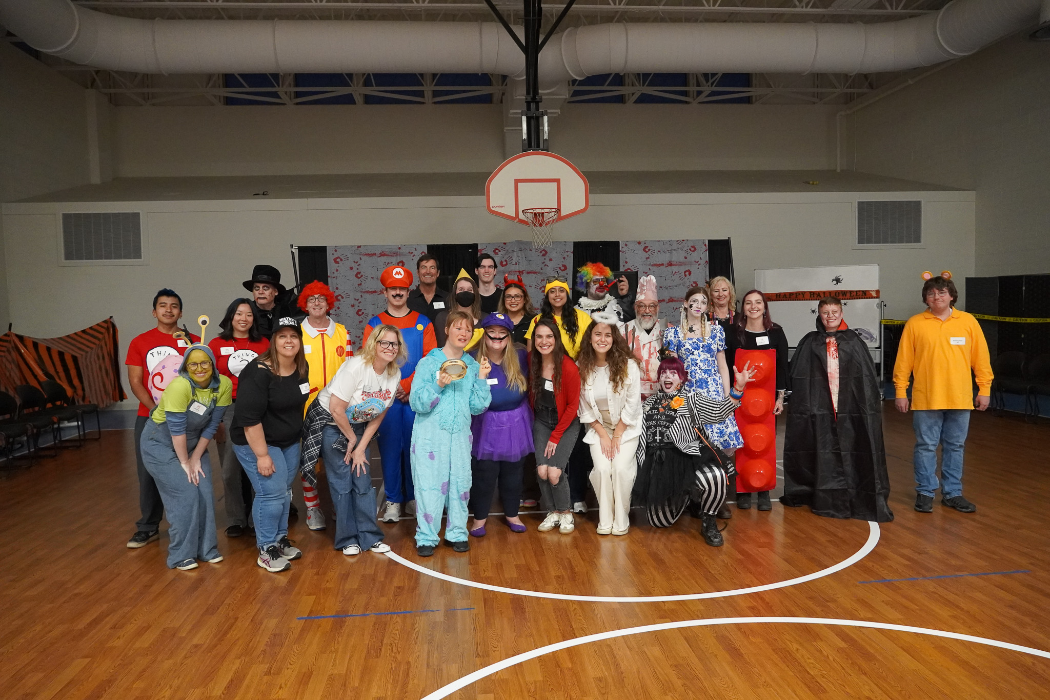 Members and staff dressed in halloween costumes pose in the gym at the Harvest Dance