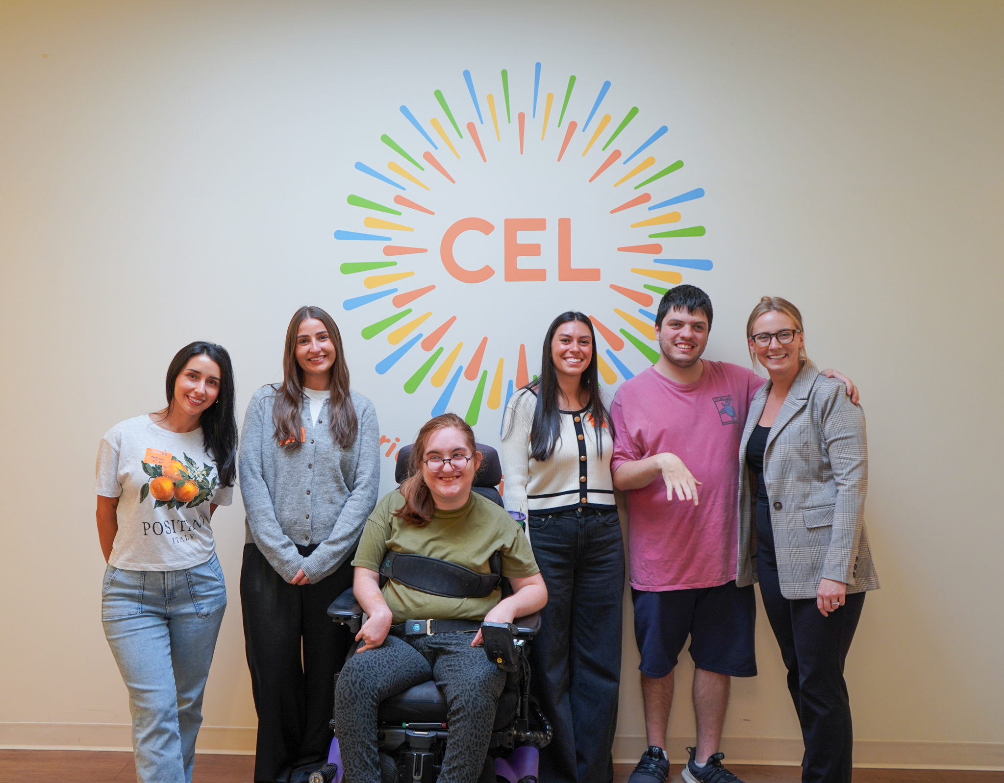 Six volunteers and members pose in front of a CEL mural